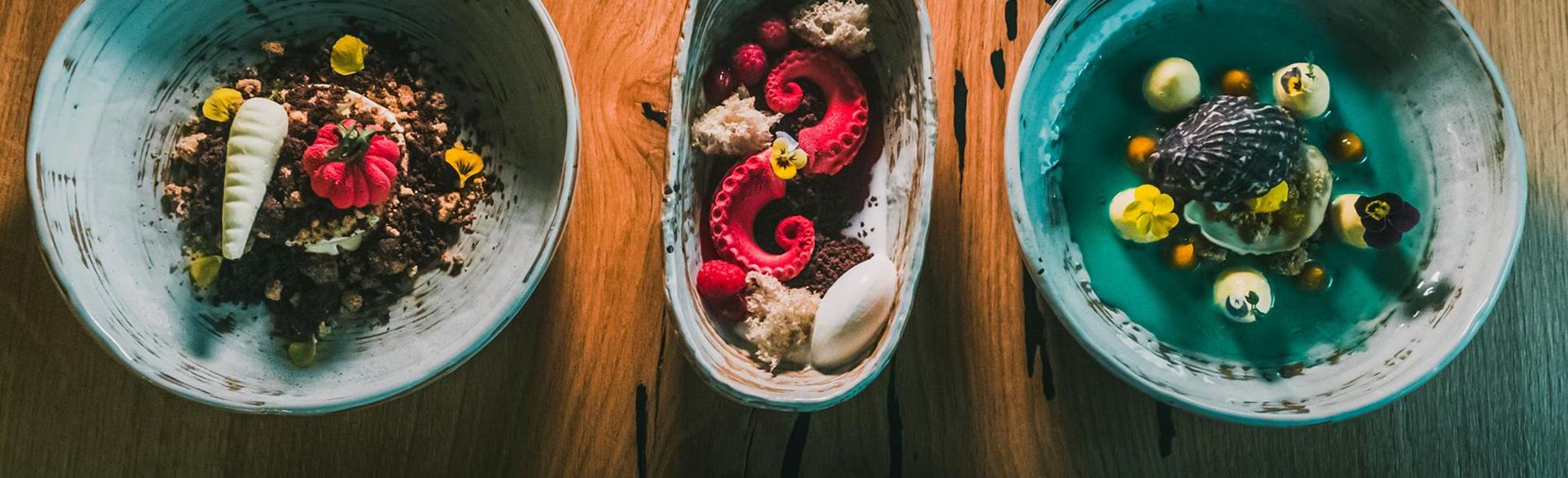 Three artfully plated desserts in ceramic bowls on a wooden table.