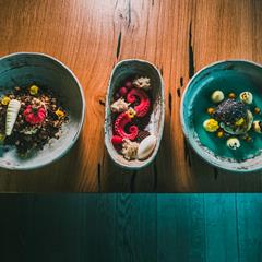 Drei kunstvoll angerichtete Desserts in Keramikschalen auf einem Holztisch.