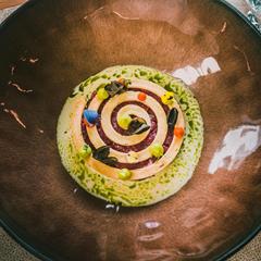 Antipasto artistico con spirale, gocce e fiori, servito in un piatto marrone.