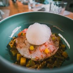 Delicate fish dish with foam, corn, and pasta served in a stylish ceramic bowl.