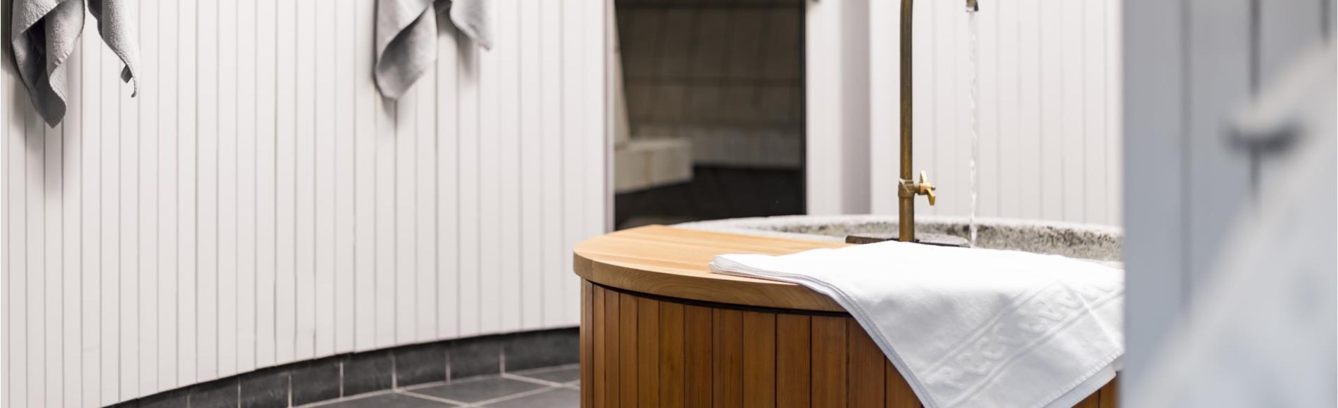 Wooden basin with running water and white towels in our elegant spa area.