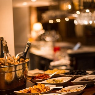 Snacks and wine bottles on a bar counter with warm lighting in the background.