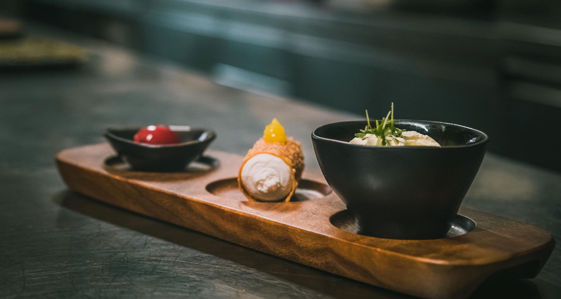 Tris di dessert su vassoio in legno con crema, cannolo e composta di frutta