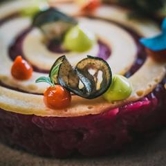 Artfully plated dish with spiral beet base, colorful vegetable creams, and zucchini chips.