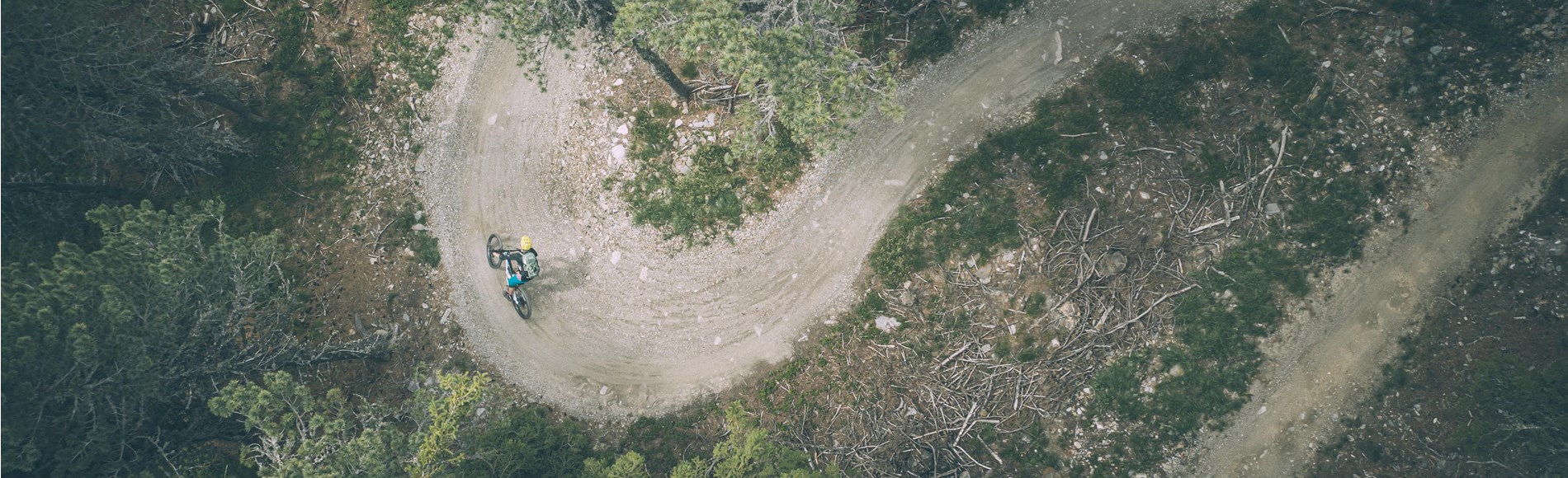 Mountain biker riding a tight curve on a forest trail, captured from above.