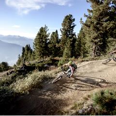 Two mountain bikers corner on a dusty forest trail with a wide view over the valley.