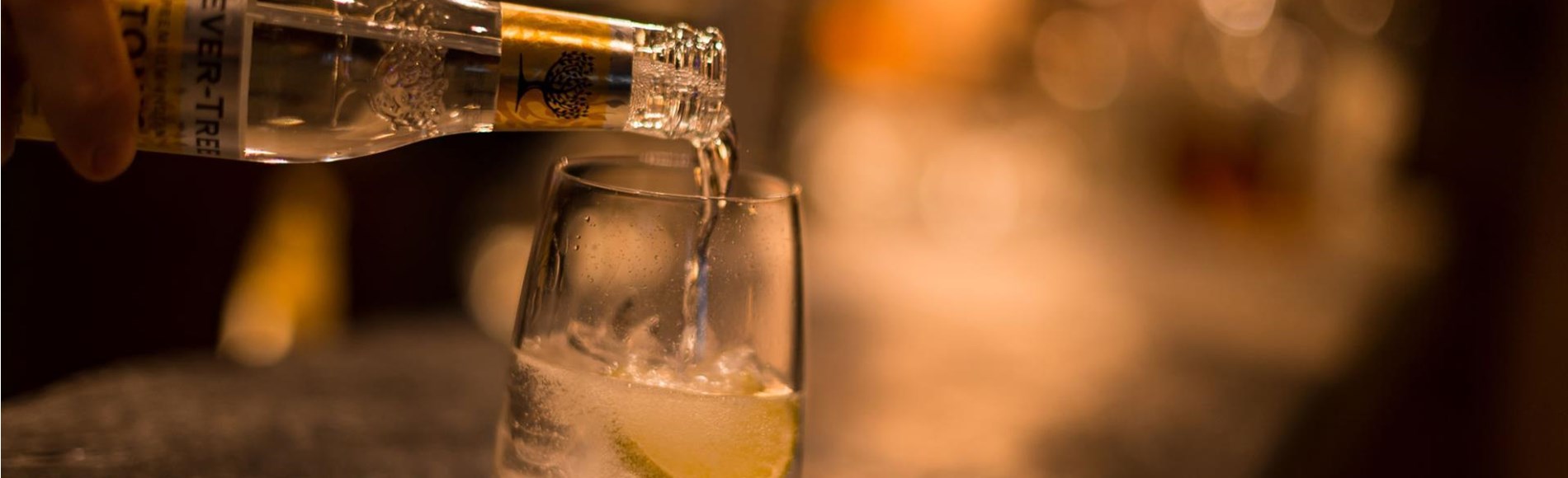 Tonic Water wird in ein Glas mit Eis und Limette gegossen